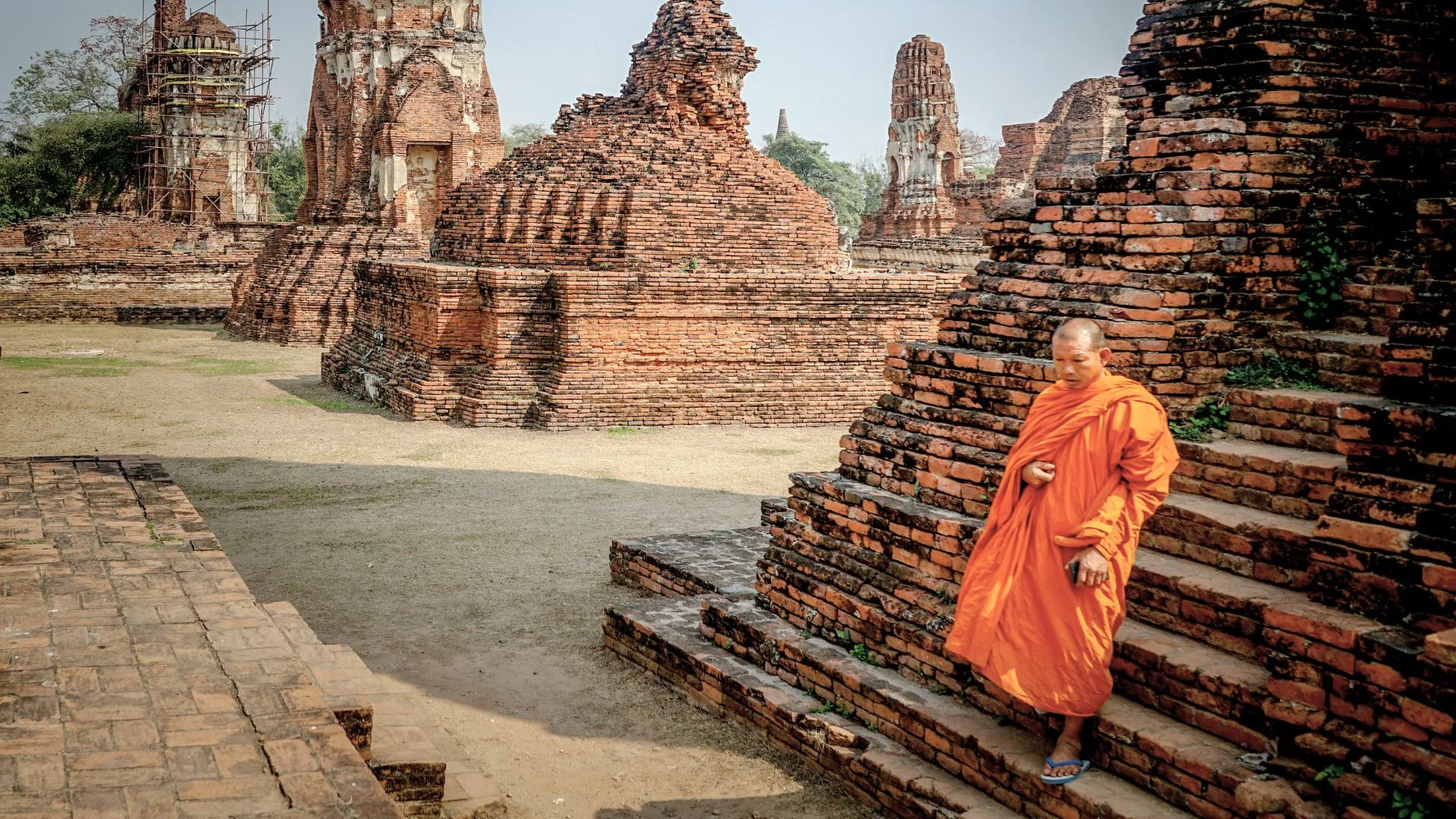 Un moine bouddhiste en robe orange devant les ruines historiques et les briques anciennes du temple Wat Yai Chai Mongkhon à Ayutthaya.